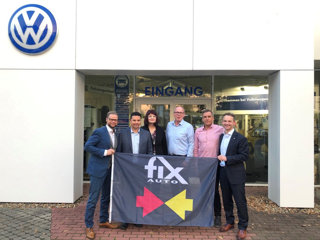 Knut Hildesheim und Mitarbeiter, Roy de Lange und Christoph Rosemeier stehen vor dem Autohaus Hildesheim und halten die Fix Auto Flagge. Oben links ist an der Fassade ein VW Zeichen