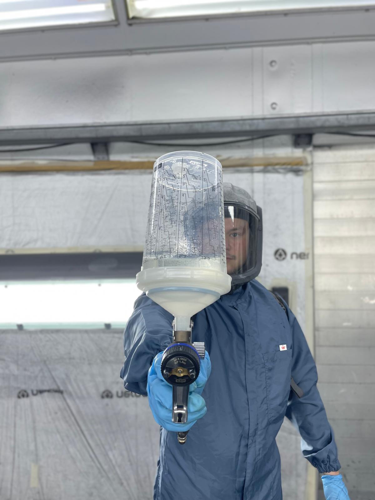 Ein Fahrzeuglackierer von Fix Auto hält eine Lackierpistole in der Hand.