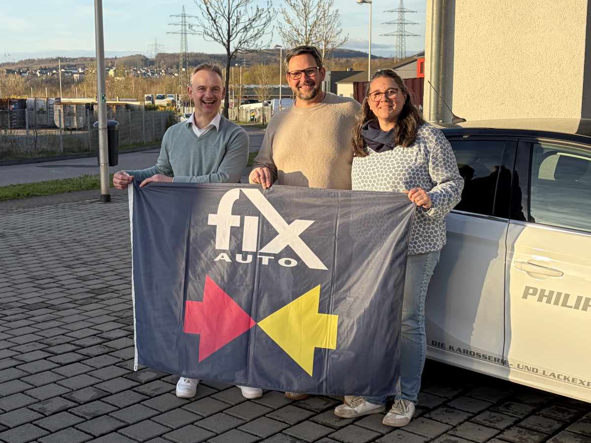 Anika und Sascha Philippi direkt nach der Vertragsunterschrift in ihrem Betrieb in Völkingen zusammen mit Roy de Lange. Roy de Lange, Sascha und Anika Philippi mit einer Fix Auto-Fahne in der Hand