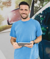 Geschäftsführer von Fix Auto Fränkische Schweiz, Martin Ploß, lächelt vor Fix Auto Hintergrund in die Kamera