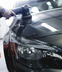 Ein Mitarbeiter poliert mit einer Poliermaschine die Motorhaube eines grauen Fahrzeugs