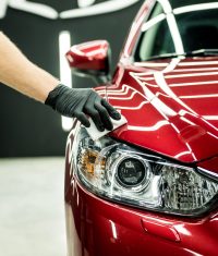 Eine Hand mit schwarzen Handschuhen reinigt die Oberfläche eines roten Fahrzeugs.