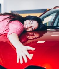 Happy beautiful young woman buying a new car at the car showroom.