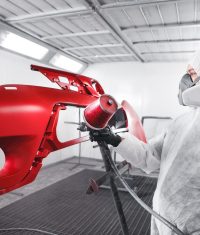 Male worker in protective clothes and mask painting car using spray paint. Body repair of the vehicle after the accident.