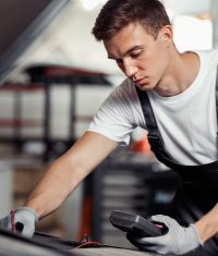 Concentrated on his job automechanic is repairing a car at a car service