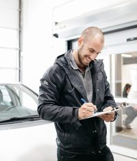 Auto body technician completing repair documentation on a clipboard inside a collision repair shop