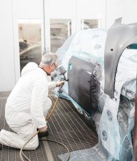 Auto body painter applying paint to a masked vehicle door inside a spray booth