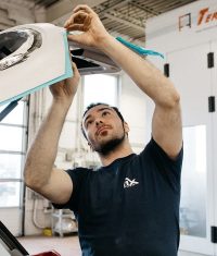 Auto body technician masking trim and preparing a vehicle panel for paint or repair